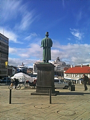 Fra sin sokkel skuer dikteren Alexander L. Kielland over torget mot Vågen som er besøkt av cruiseskip i sommerhalvåret. Se full tekst nederst på siden.